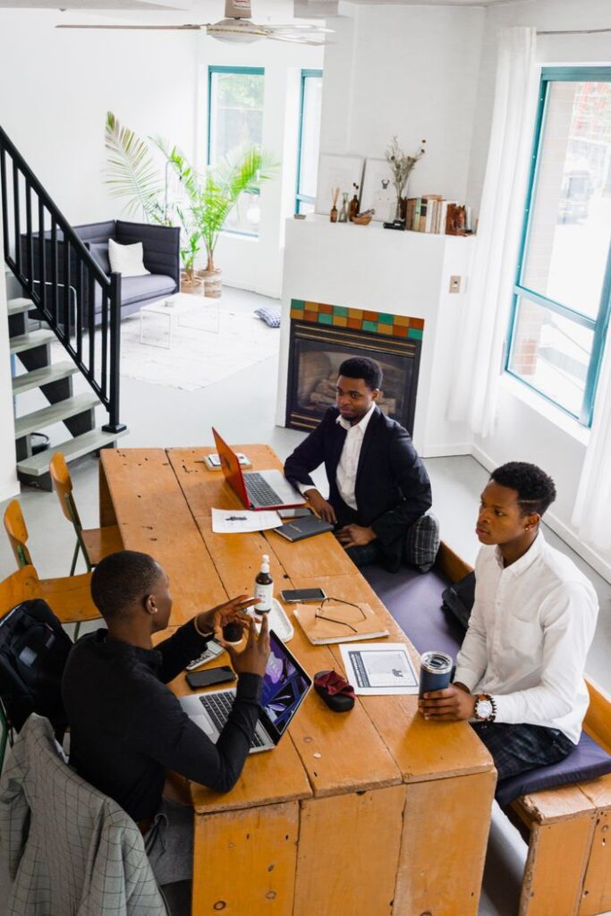 Three colleagues engaged in a discussion around a wooden table in a bright office setting.